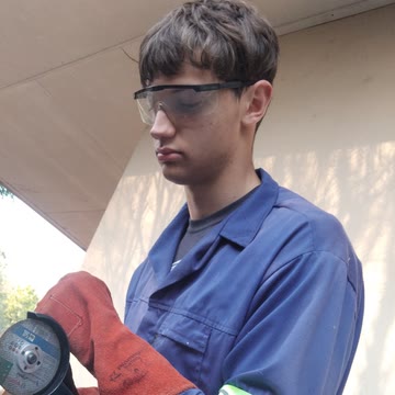 Alex van Heerden cutting steel in the workshop, in overalls and safety glasses