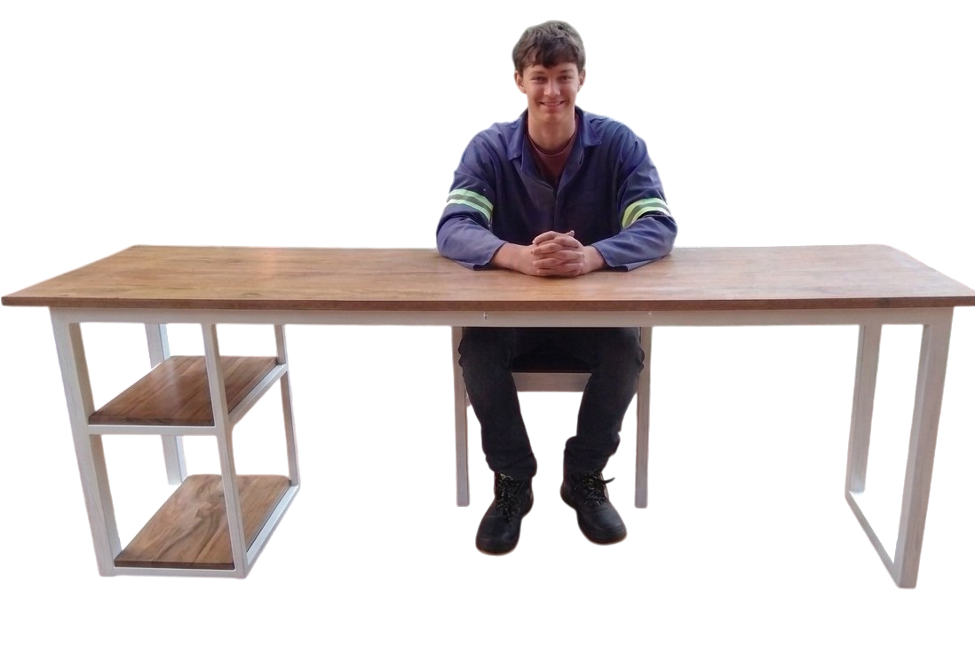 The same desk design after it was built — welded steel frame, board top, side shelves, with Alex sitting at it