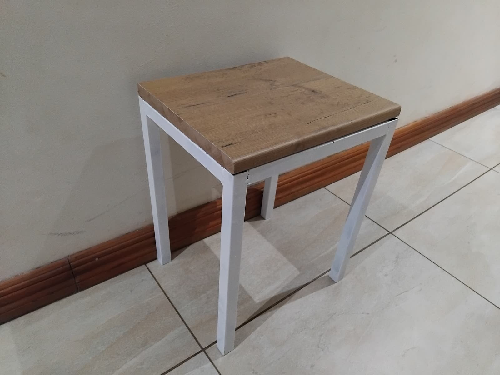 A small square side table with a white steel frame and an oak-look top, against a wall